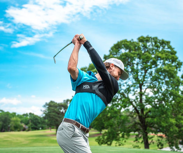 Male golfer during backswing on golf course, side view wearing Kinetic Arm K2 Sleeve, highlighting MuscleWeb® support polymers and sleeve design.
